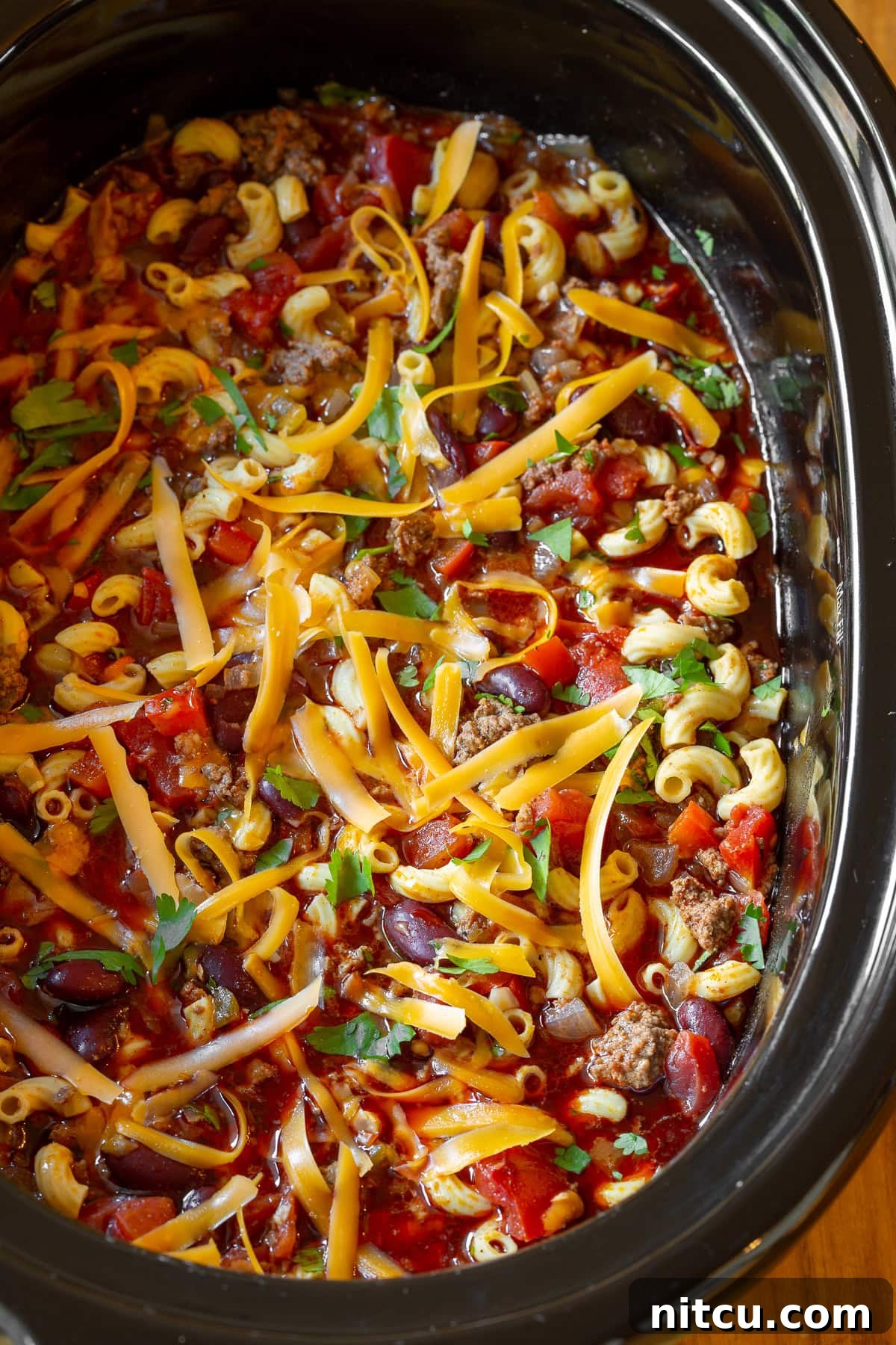 A close-up, top-down view of Slow Cooker Chili Mac and Cheese, garnished with a generous sprinkle of shredded cheese and fresh cilantro, ready to be served.