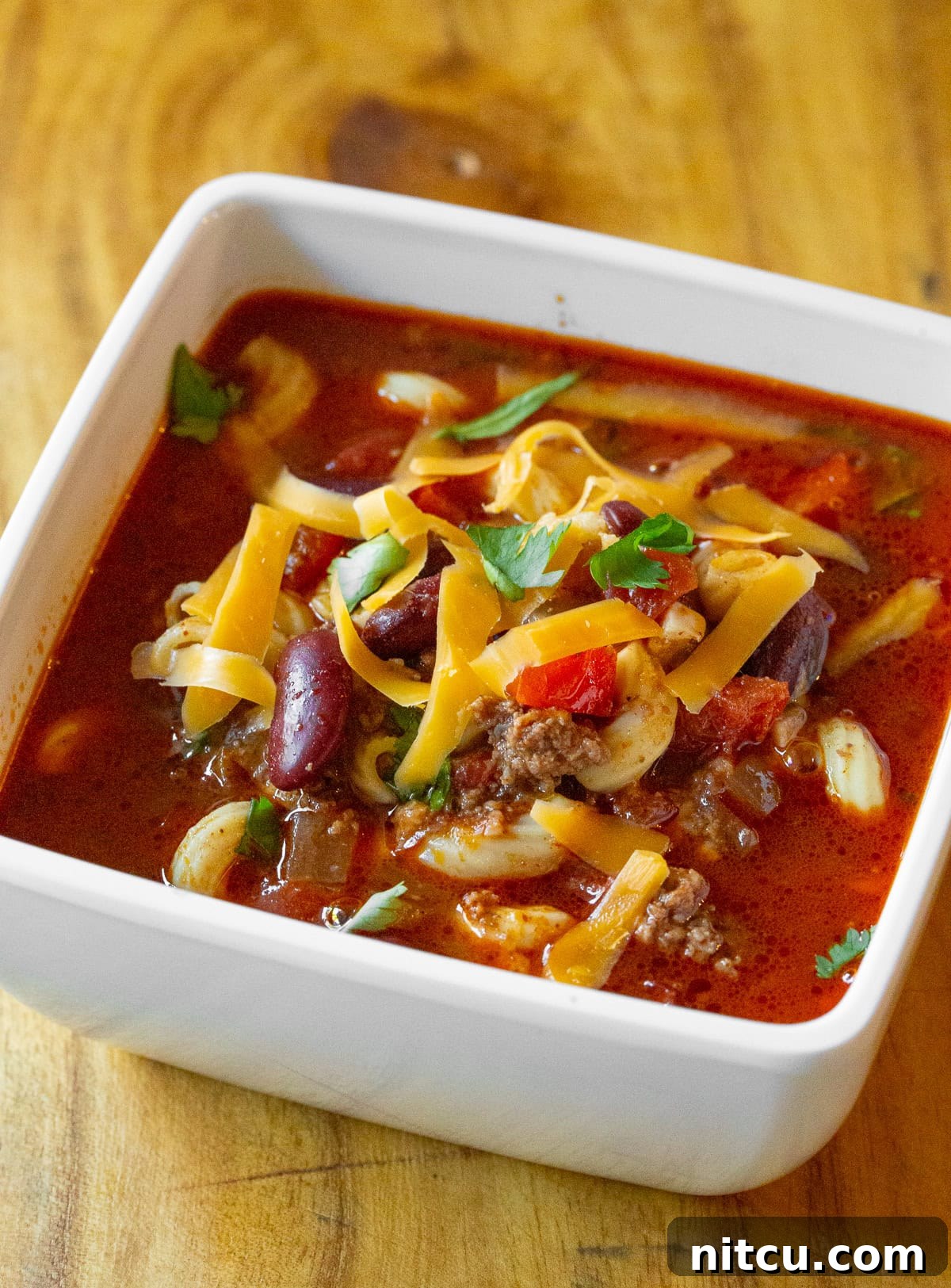 A vibrant single serving of Slow Cooker Chili Mac and Cheese, showcasing the perfectly cooked macaroni noodles, kidney beans, colorful vegetables, melted cheese, and fresh cilantro garnish.