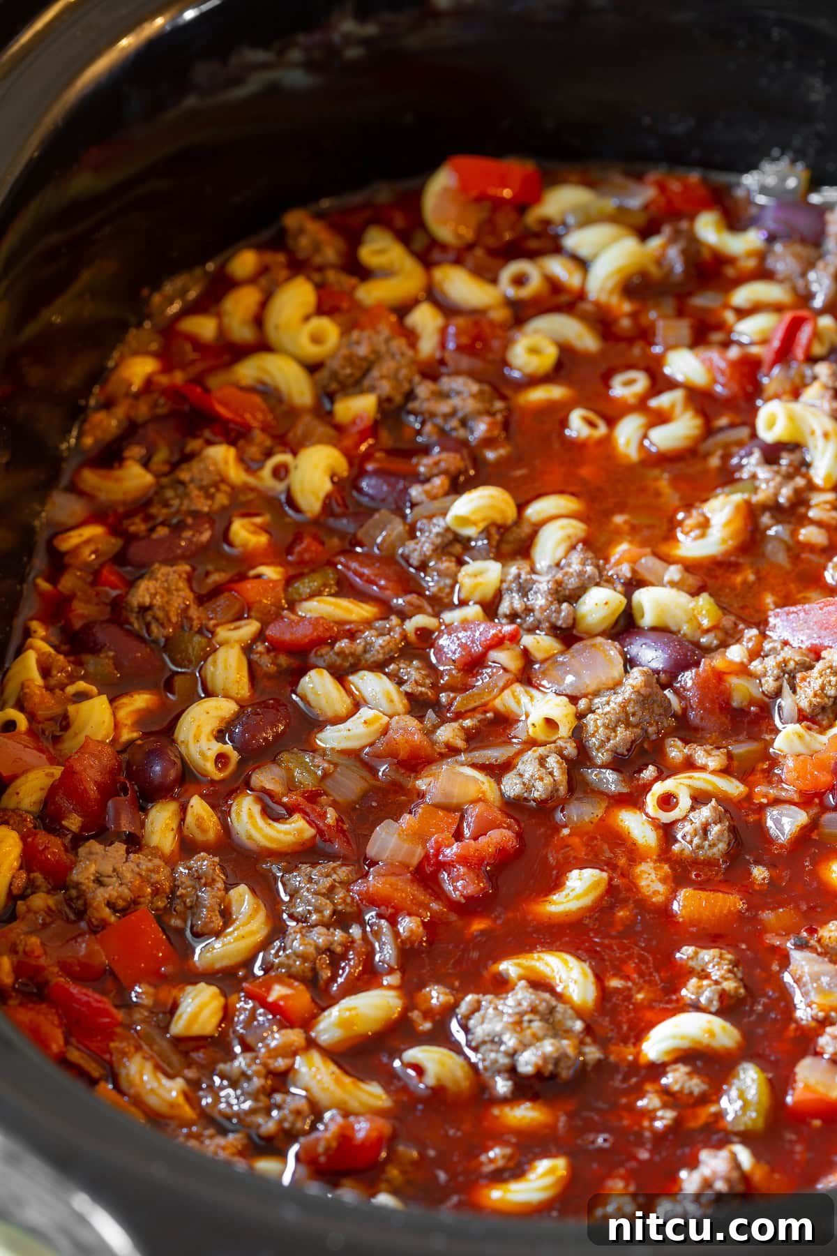 The Slow Cooker Chili Mac and Cheese simmering in the pot, rich with meat, beans, and spices, before the final addition of macaroni and cheese.