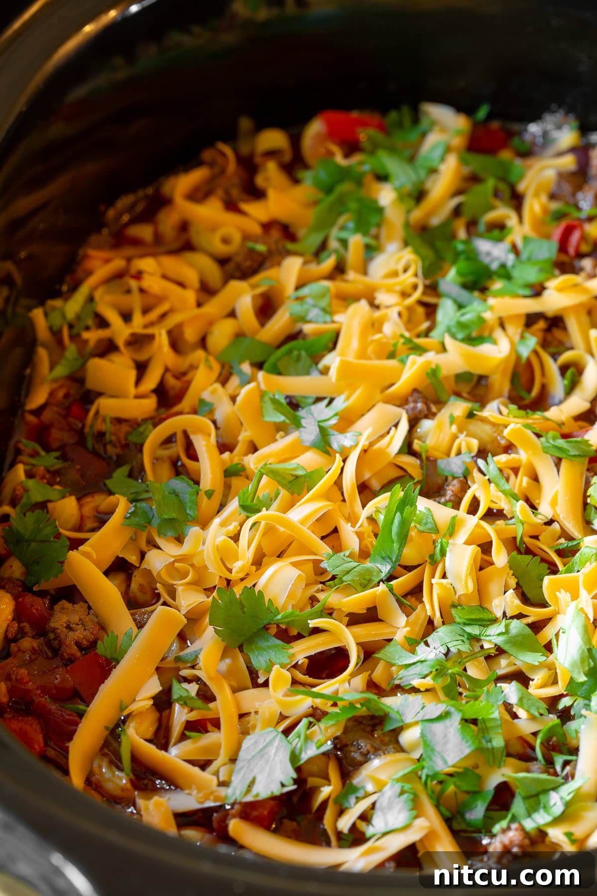 A generous serving of Slow Cooker Chili Mac and Cheese, richly topped with an abundance of shredded cheddar cheese and fresh green cilantro, ready to be enjoyed.