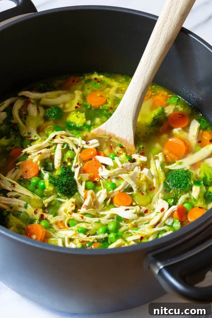 A large pot of simmering chicken detox soup, stirred with a wooden spoon, showcasing a rich blend of brightly colored vegetables and a golden broth.