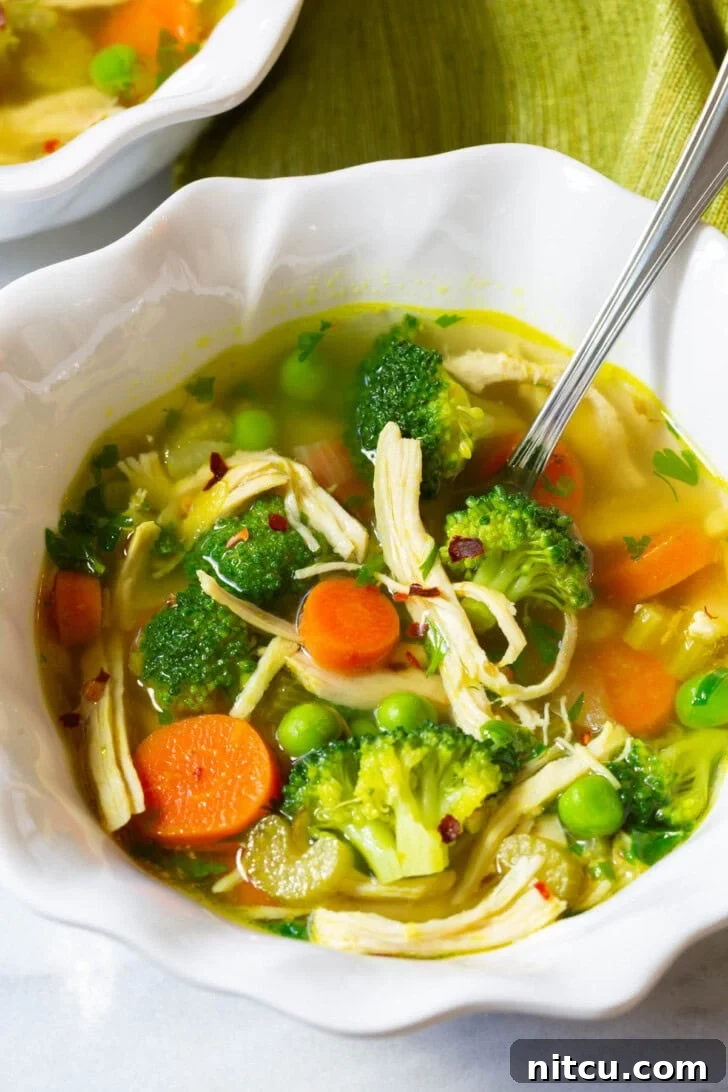 A single bowl of vibrant chicken detox soup, garnished with fresh herbs, with a spoon nestled inside, perfectly ready to be eaten.