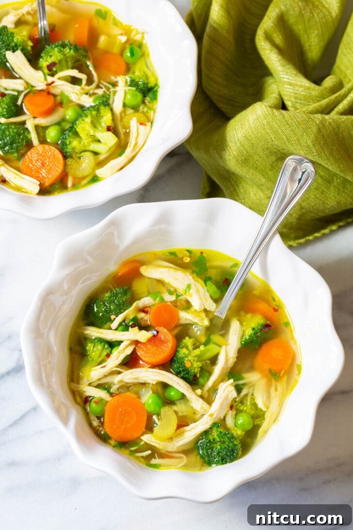 Two pristine white bowls, brimming with steaming chicken detox soup, garnished with vibrant fresh herbs, ready to serve and nourish.