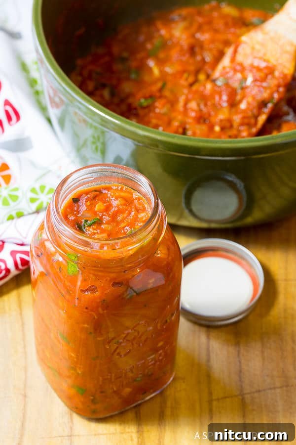 A clear glass mason jar showcasing beautifully rich, homemade marinara sauce, ready for storage or serving.