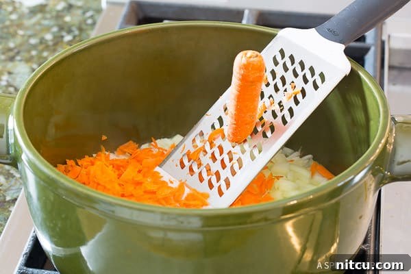 Close-up shot of shredding fresh carrots directly into a green cooking pot, ready to be incorporated into the sauce.