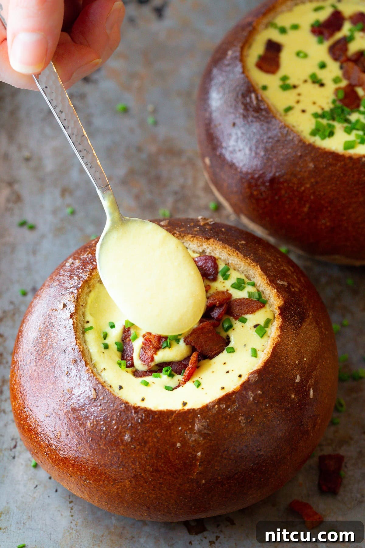 Spoon lifting a creamy bite of Irish Beer Cheese Soup from a bread bowl.