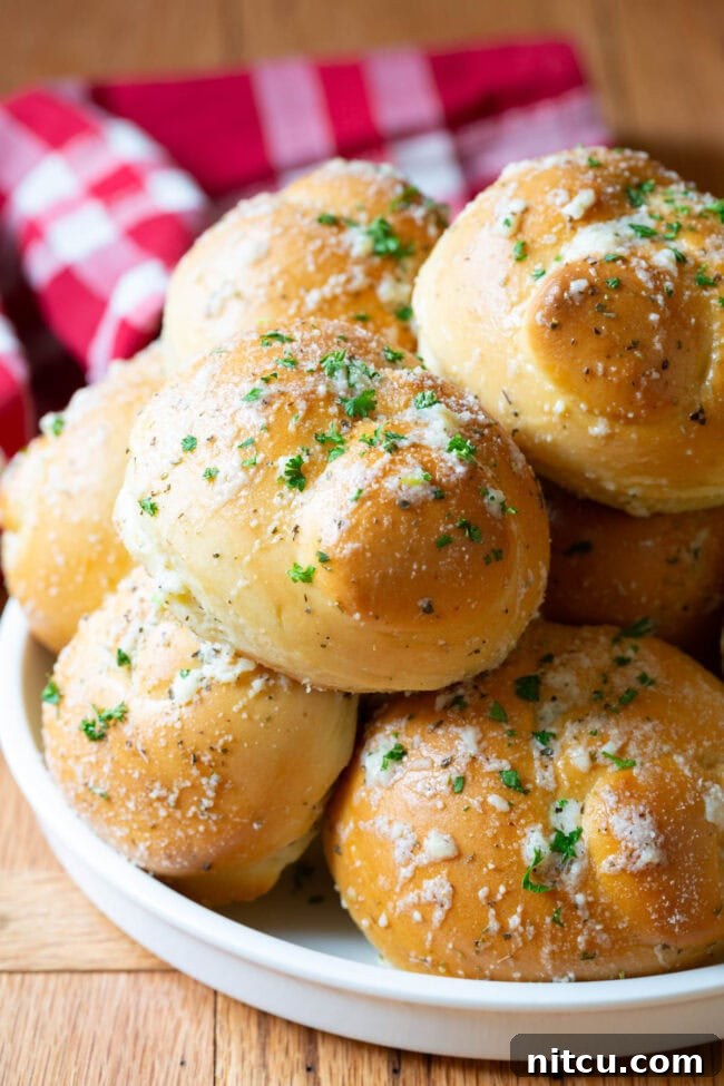 Effortless Garlic Knots 2 Garlic knots piled on top of each other on a white plate, showcasing their golden-brown crust and glistening garlic butter.