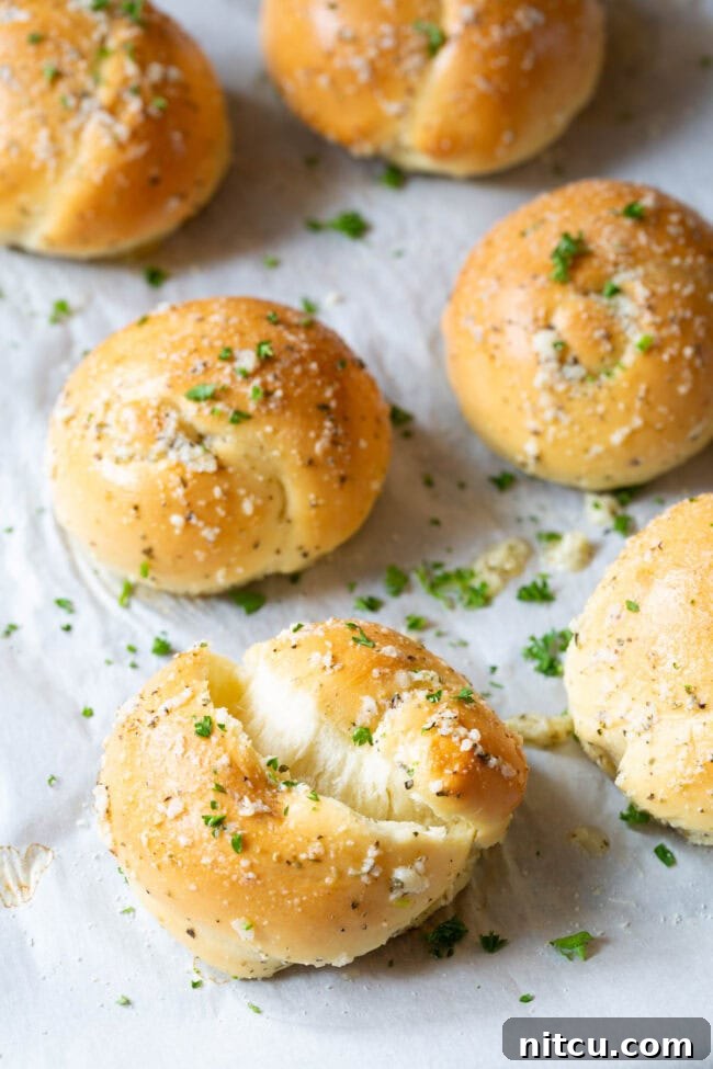 Effortless Garlic Knots 11 One garlic knot ripped to show its fluffy interior, with the rest of the batch lying behind it on a baking sheet.