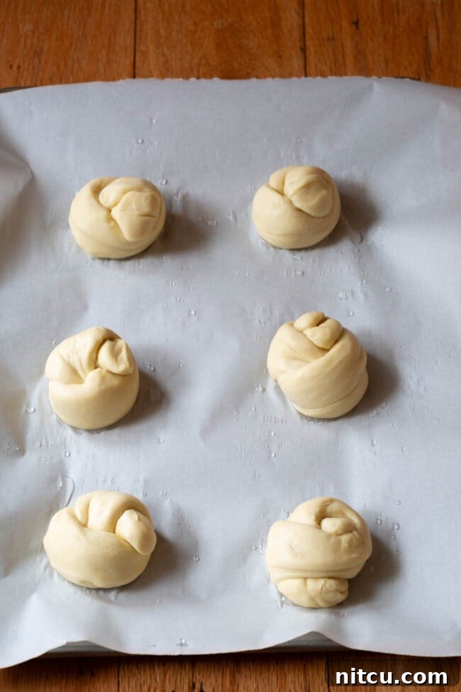 Effortless Garlic Knots 7 Garlic knots rising on a baking sheet, appearing plump and ready for their final bake.