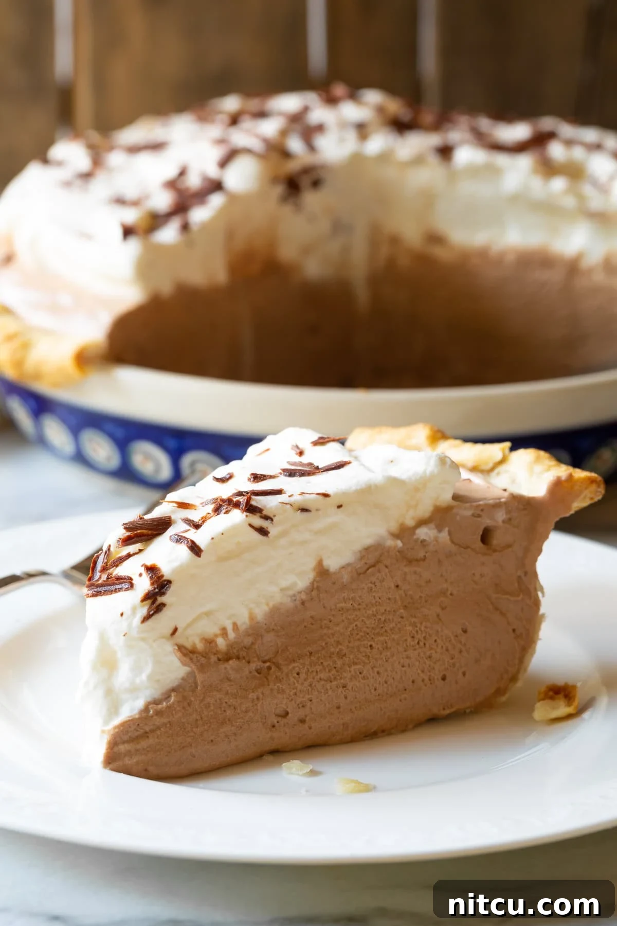 French Silk Pie #ASpicyPerspective #FrenchSilkPie #SilkPie #FrenchSilkPieRecipe #ChocolateSilkPie #Chocolate #Silky #Fluffy #Pie #Dessert Close-up of a slice of French Silk Pie on a plate, showing its silky texture and whipped cream.