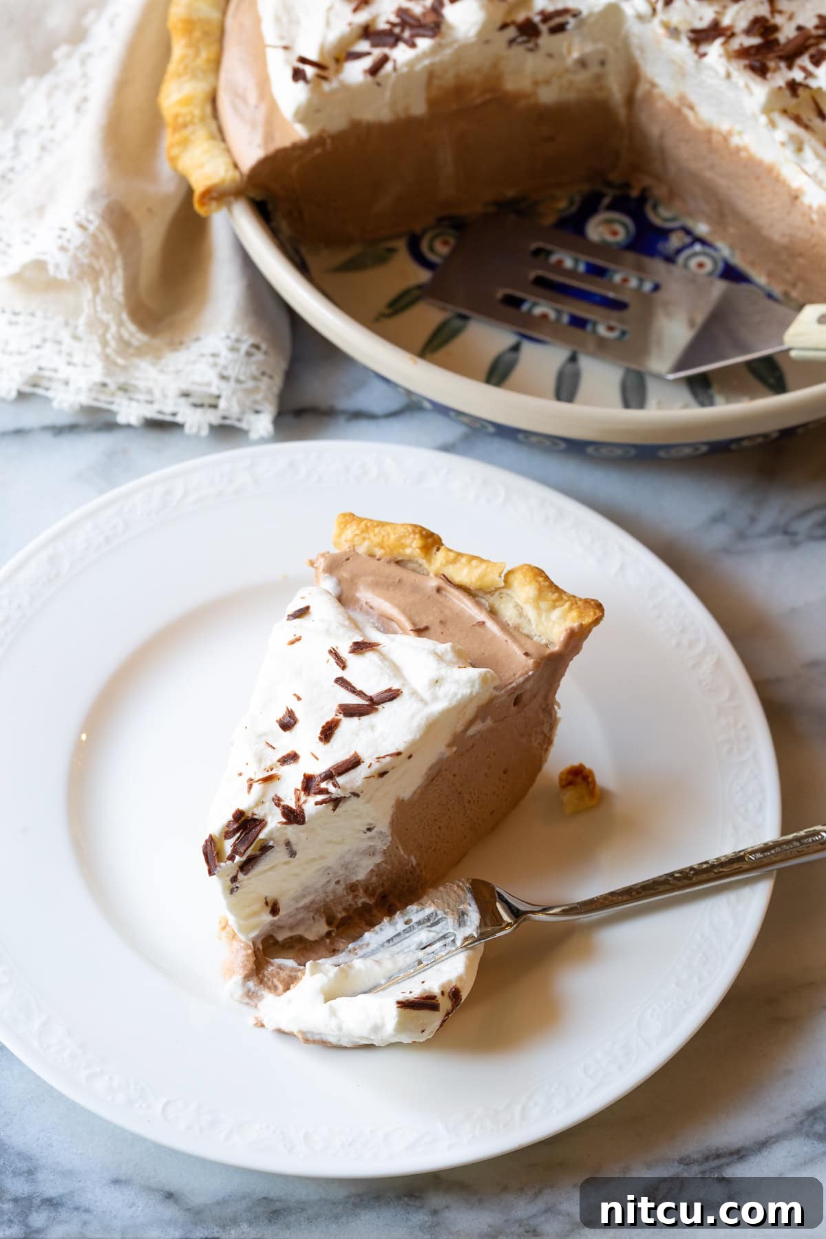 French Silk Pie #ASpicyPerspective #FrenchSilkPie #SilkPie #FrenchSilkPieRecipe #ChocolateSilkPie #Chocolate #Silky #Fluffy #Pie #Dessert A single slice of chocolate cream pie, showcasing its perfect layers and smooth texture.