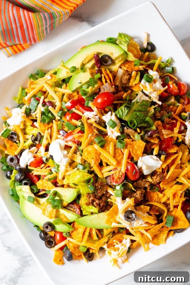 Legendary Dorito Taco Salad 12 A beautifully arranged Dorito taco salad, overflowing with crisp lettuce, vibrant grape tomatoes, black olives, green onions, avocado slices, and shredded cheddar cheese, adorned with multiple dollops of creamy ranch sour cream around the edges.