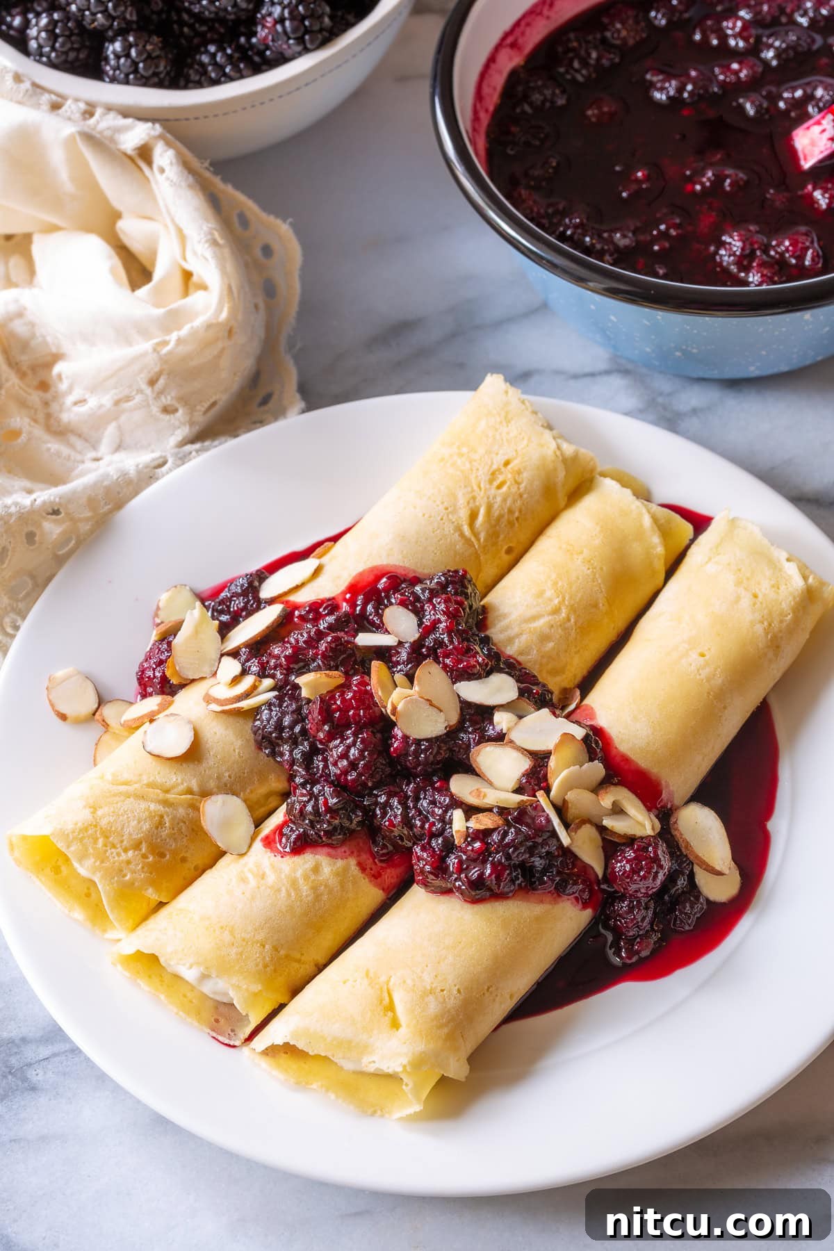 Golden Cheese Blintzes 2 Blintz pancakes resting on a white plate with blackberry sauce, garnished with almonds