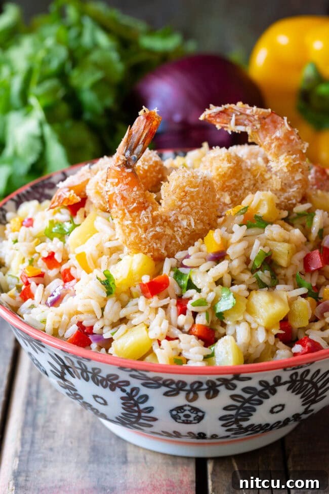 Caribbean Confetti Rice #ASpicyPerspective #Rice #Caribbean #CaribbeanRice #CaribbeanRiceRecipe #ConfettiRice #SideDish #Jalapenos #Pineapple #BellPeppers #CoconutMilk Caribbean Rice in a bowl with coconut shrimp on top.