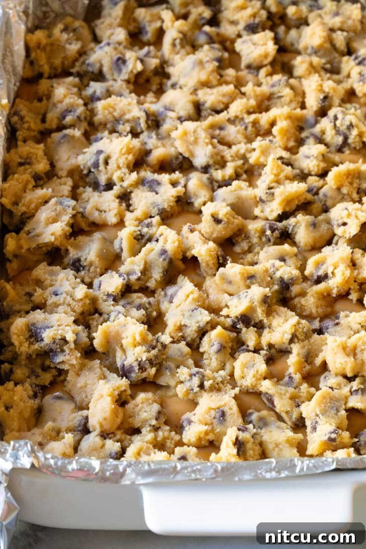 Cookie dough pieces on top of caramel in a baking dish lined with foil. 