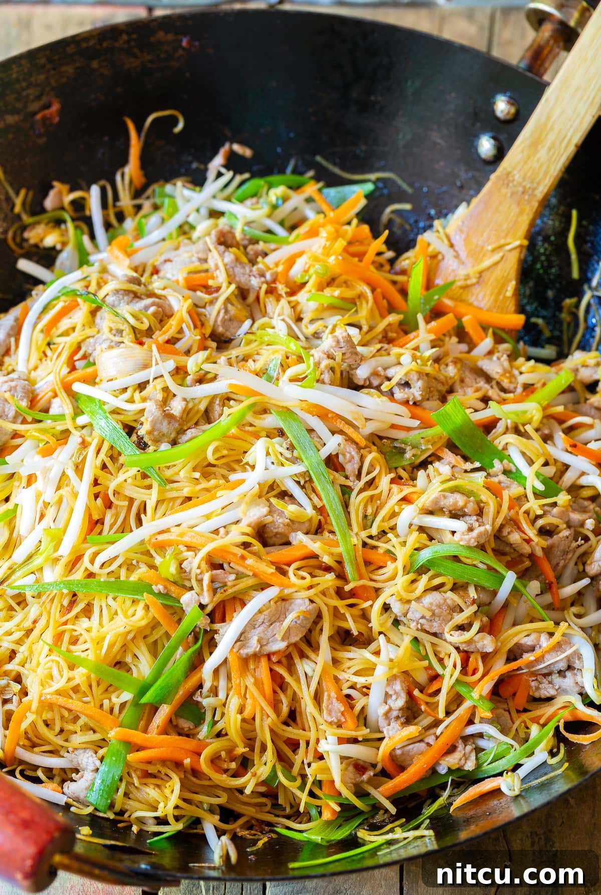 Savory Cantonese Pork Noodles 3 Close-up of Pork Lo Mein (Cantonese Noodles) being stir-fried in a traditional wok, showcasing the steam and rich colors of the ingredients.