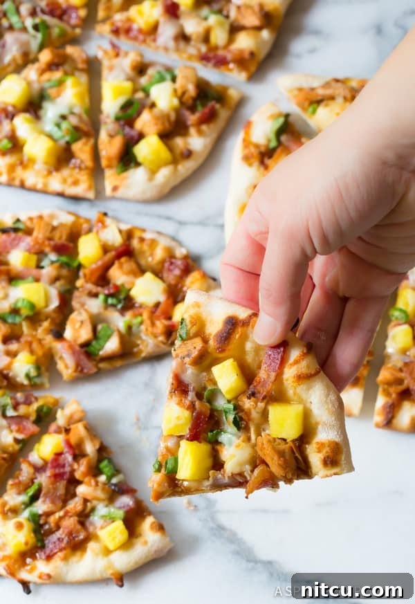 Umami Grilled Teriyaki Chicken Pizza 11 Chicken Teriyaki Pizza - lifting a piece with a hand, showing the crispy crust and melted cheese.