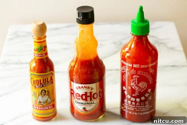 The Encore Sauce 4 Three distinct bottles of hot sauce lined up neatly on a pristine marble countertop, ready for use.