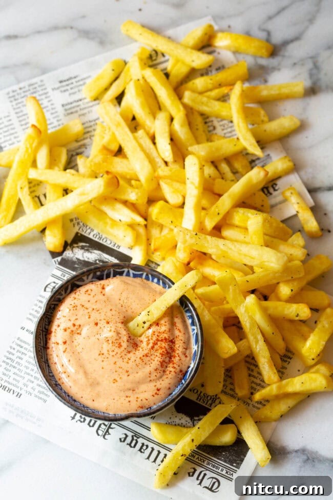 The Encore Sauce 6 A hand dipping a crispy French fry into a bowl of luscious Southern Comeback Sauce, with more fries and a newspaper background.