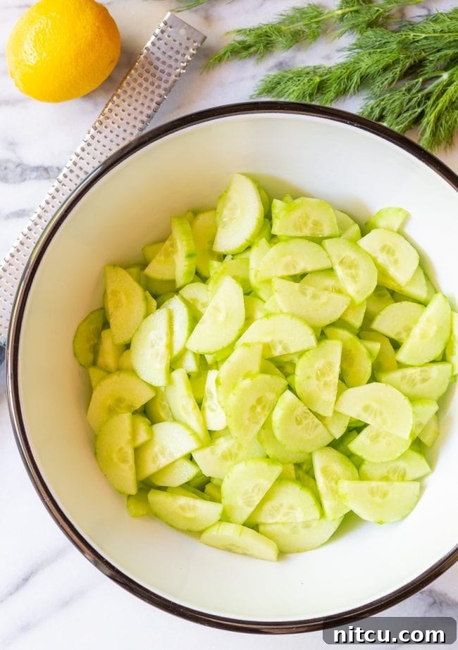 Perfectly sliced cucumbers ready for a refreshing salad. Top view of thinly sliced English cucumbers, perfectly halved and ready for mixing in a large bowl, showcasing their crisp texture.