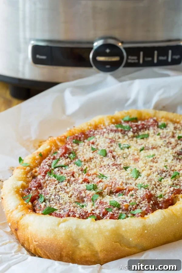 A side view of a glorious crockpot pizza, with its thick, golden crust and abundance of toppings, presented on a piece of parchment paper next to the slow cooker.