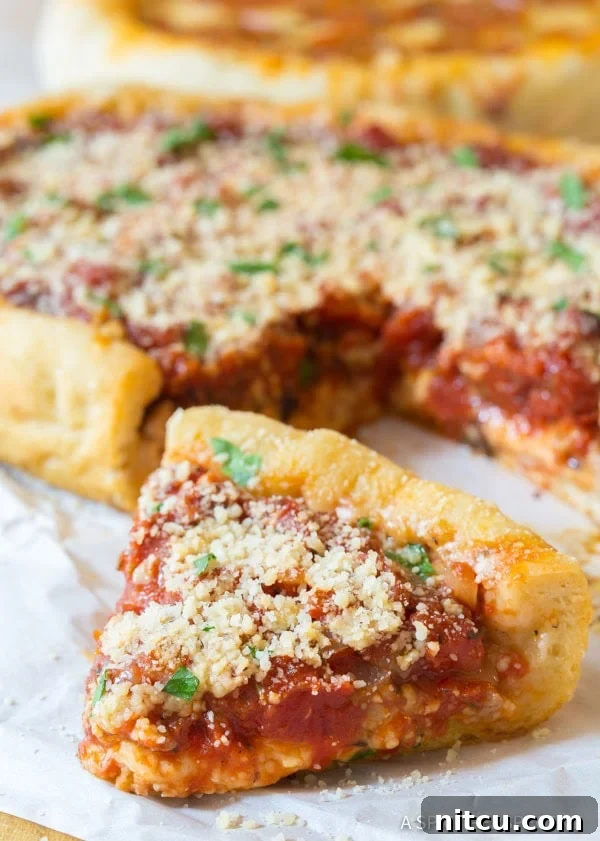A delectable slice of slow cooker deep dish pizza, showcasing its impressive layers of cheese, sausage, and sauce, resting on parchment paper with the remaining pizza blurred in the background.