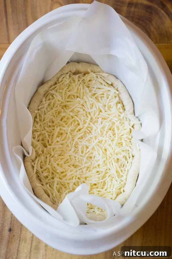 A top-down view of the pizza crust with a generous layer of shredded cheese at the bottom of the crockpot.
