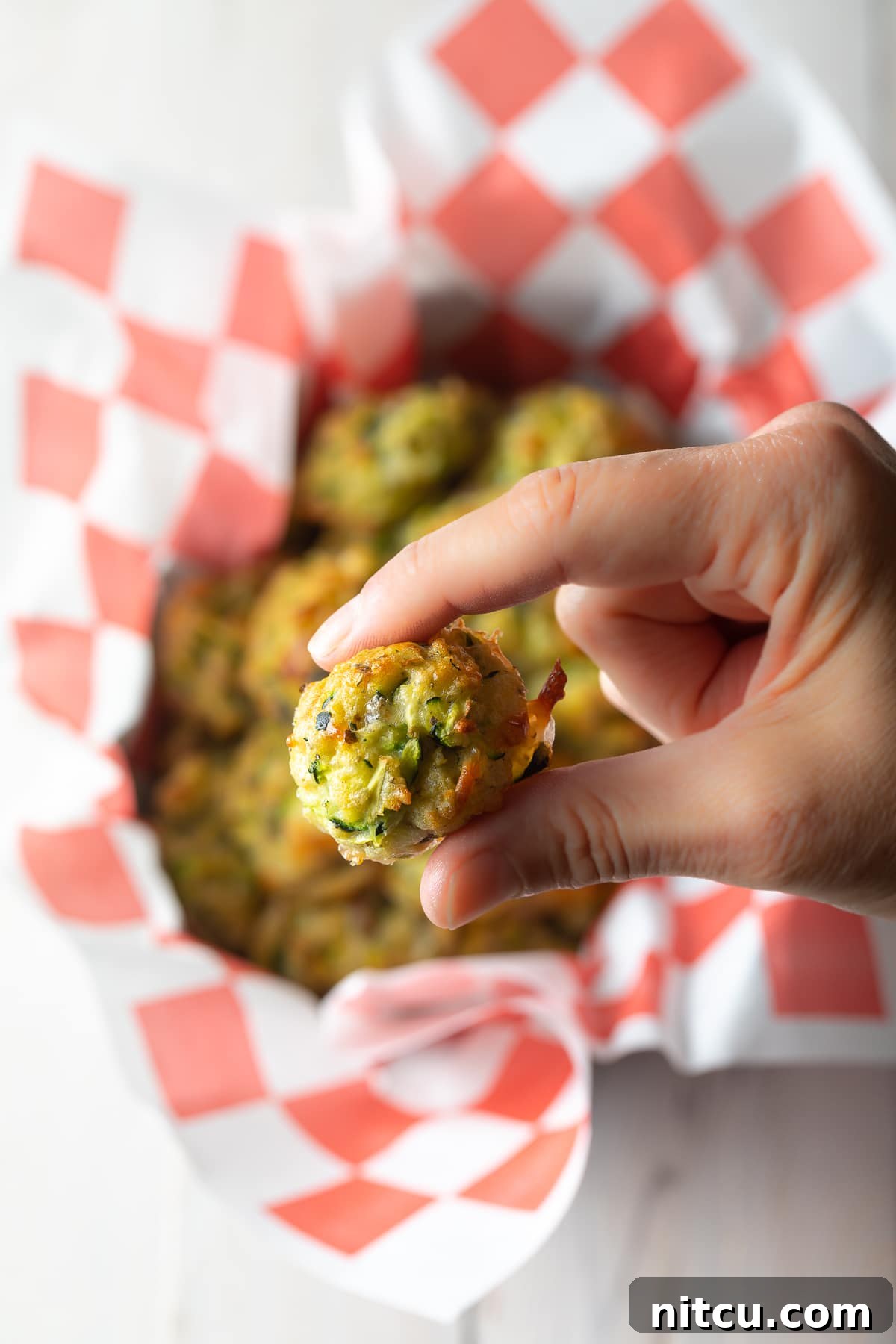 Crispy Zucchini Bites 3 A hand gently holds a perfectly baked zucchini tot, showcasing its golden-brown texture.