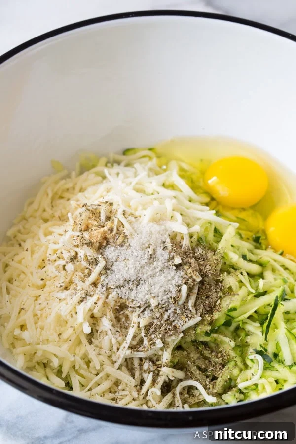 Crispy Zucchini Bites 5 A bowl filled with fresh ingredients for zucchini tots, including shredded zucchini, cheese, and spices.