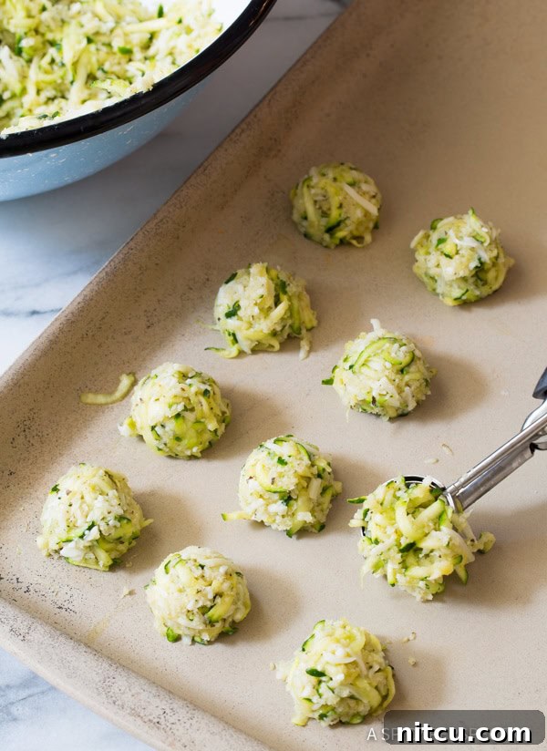 Crispy Zucchini Bites 6 Uniform balls of zucchini tot mixture perfectly spaced on a parchment-lined baking sheet, ready for the oven.