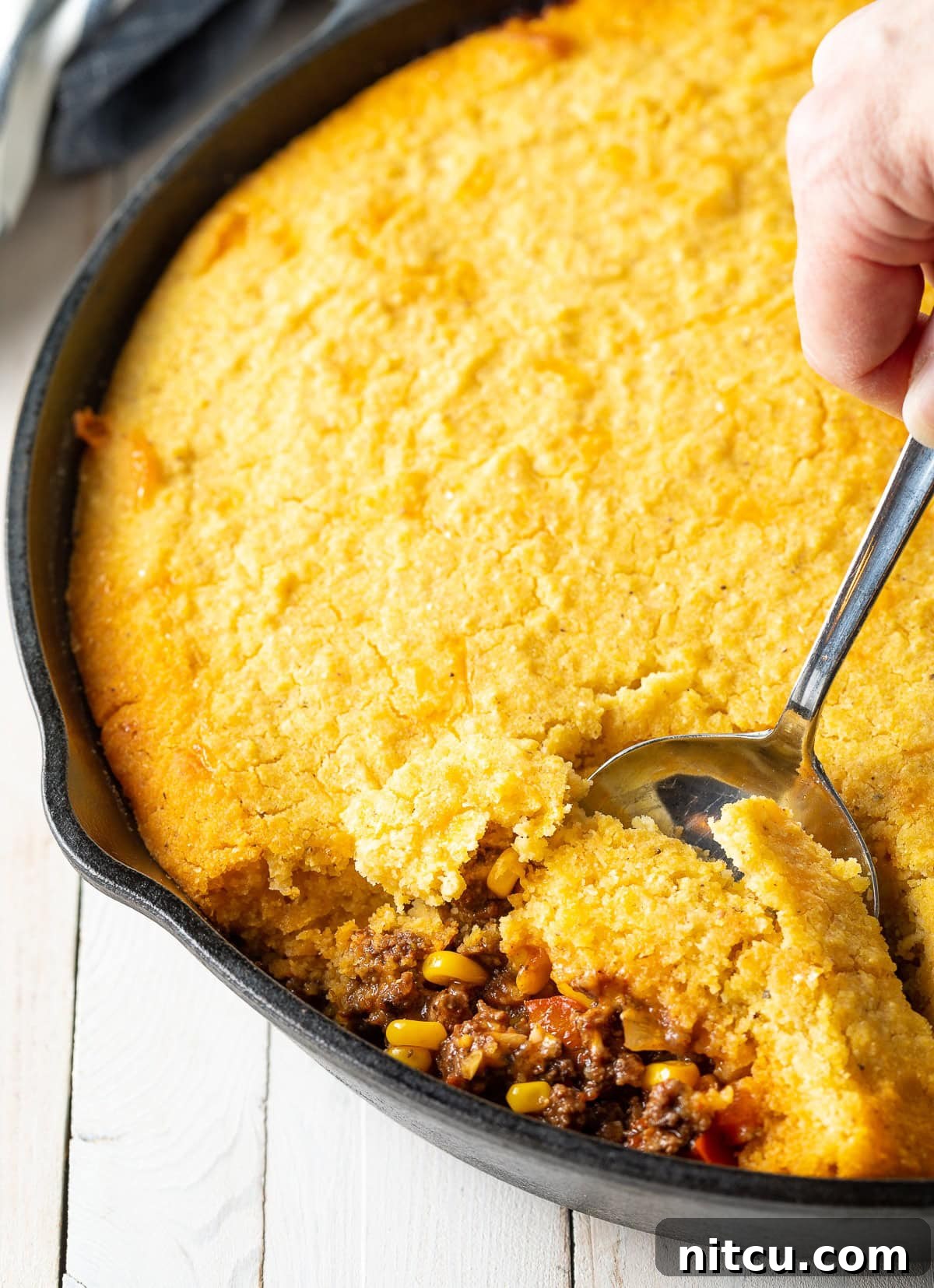 Tamale pie in a cast iron skillet with a spoon taking a portion. 