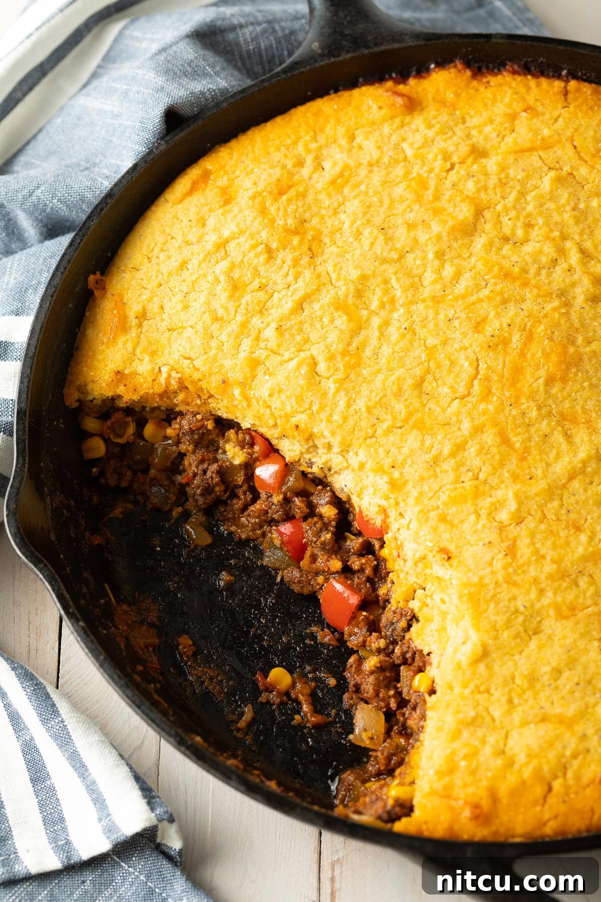 Overhead shot of tamale pie in a cast iron pan with a portion gone to show the layers. 