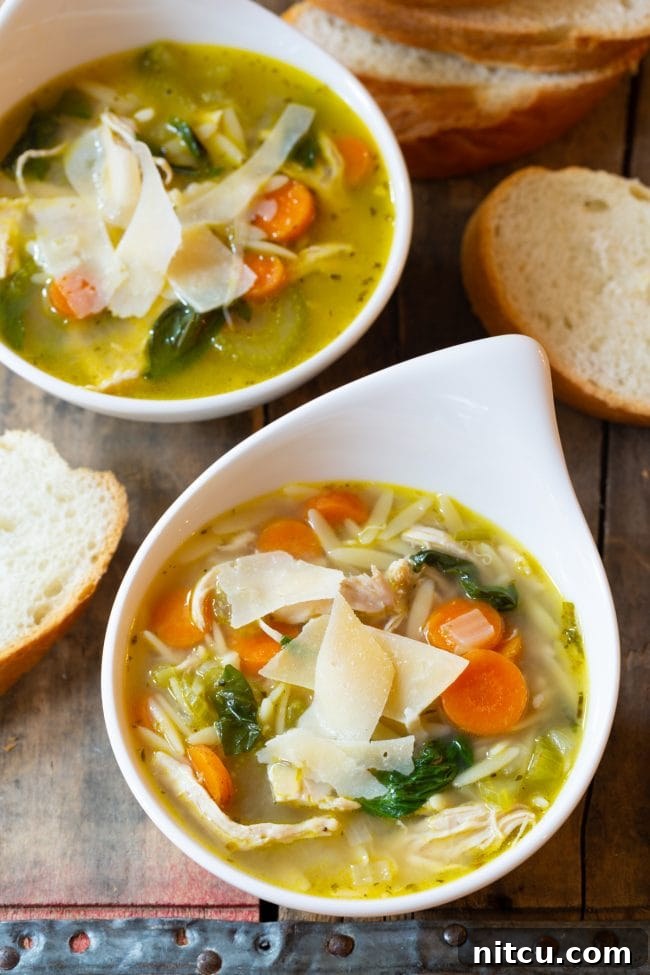 Overhead shot of two bowls of Italian chicken orzo soup with slices of crusty bread and fresh herbs scattered around.