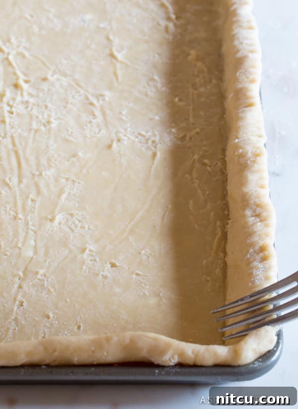 Ultimate Autumn Pumpkin Slab 3 Crimping the edges of a homemade pie crust in a cookie sheet, a crucial step for a beautiful slab pie.