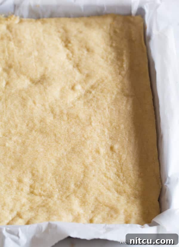Pecan-Bars-Preparation Buttery shortbread cookie crust resting in a baking pan, perfectly lined with parchment paper.