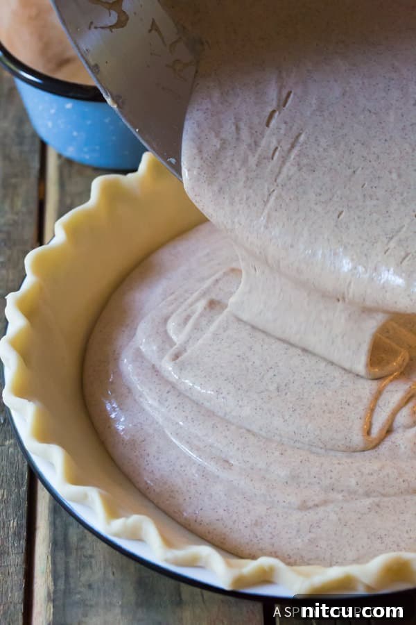 Cinnamon pie filling being poured into a pie pan lined with pie crust. 