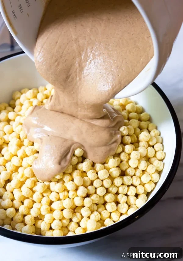 Coating Kix cereal with melted white chocolate and peanut butter for Snowball Party Mix