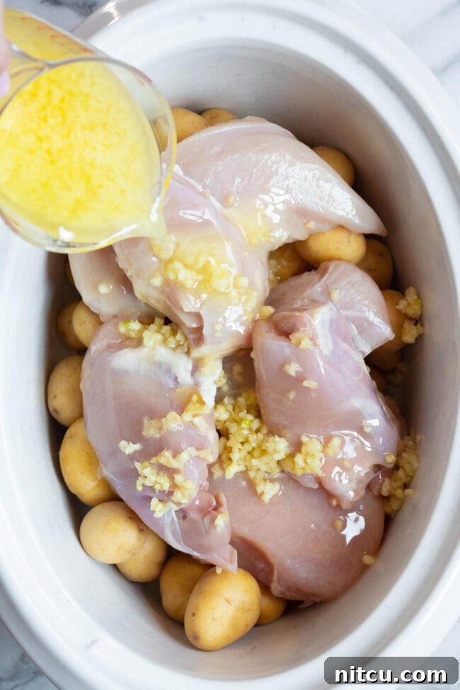 Tender Garlic Butter Slow Cooker Chicken and Potatoes 4 Raw chicken and potatoes arranged in a slow cooker, with a luscious garlic butter mixture being generously poured over the ingredients.