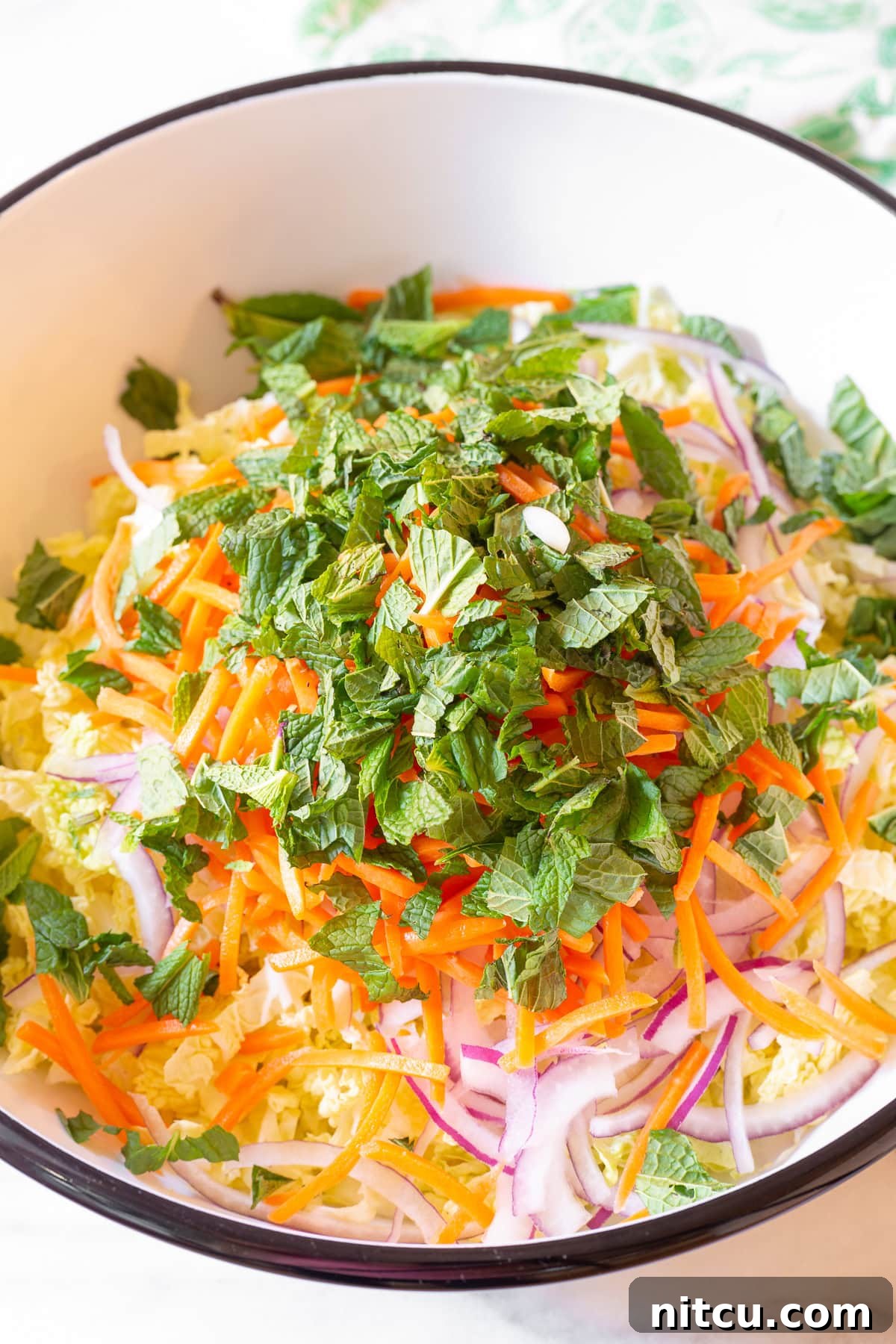 A large mixing bowl filled with crisp vegetables, including shredded lettuce, vibrant red cabbage, thinly sliced onions, and bright orange carrots, ready to be combined for the Vietnamese Chicken Salad.