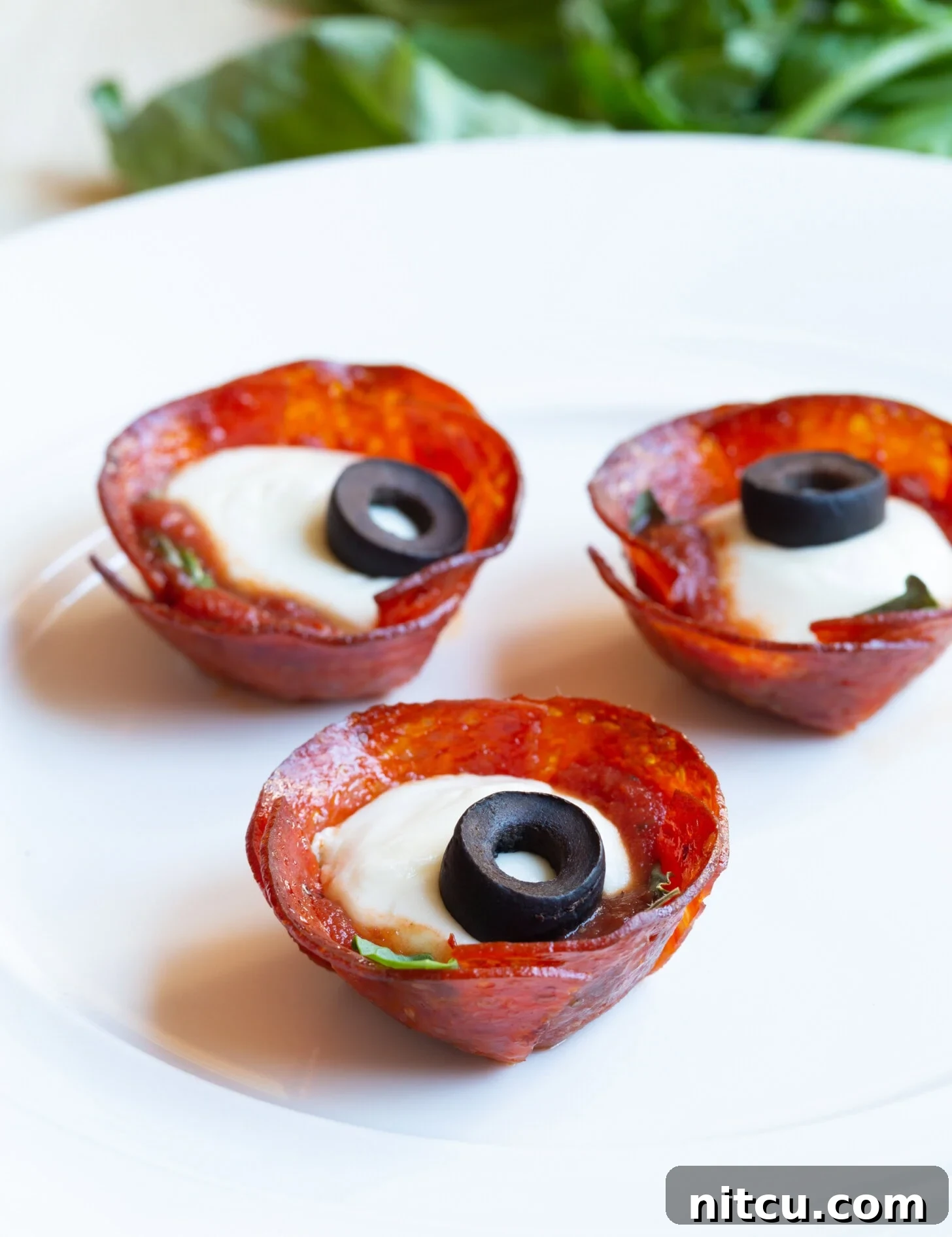 Irresistible Low-Carb Pepperoni Pizza Bites: The Ultimate Cheesy & Crispy Party Appetizer for Game Day & Beyond A plate brimming with golden-brown, cheesy pepperoni cups, garnished with vibrant green basil and savory black olives, ready to be served as an irresistible appetizer.