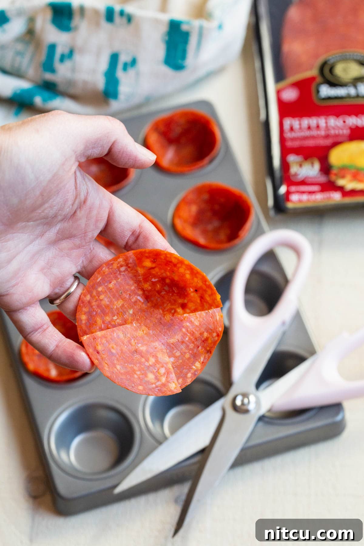 Savory Pepperoni Crisps 3 A hand holds a large pepperoni slice, expertly cut with kitchen scissors to create four slits around the edge, ready to be shaped into a cup.