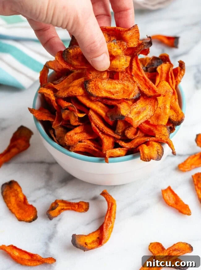 Crunchy Carrot Chips A hand reaching into a bowl to grab a handful of delicious carrot chips.