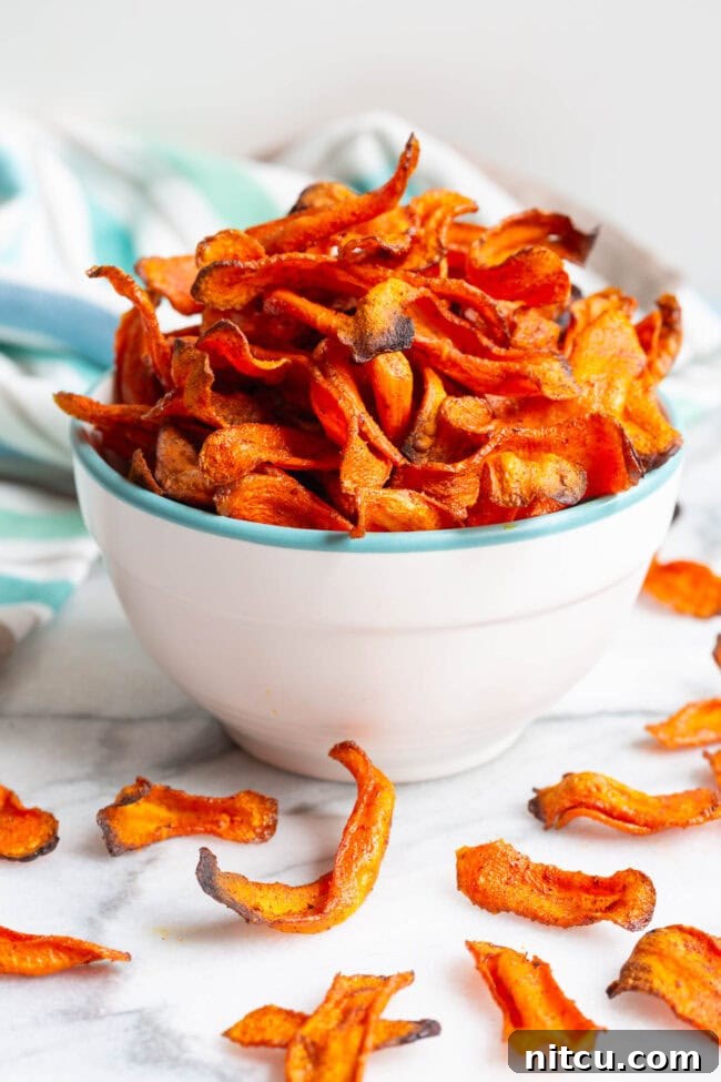 Crunchy Carrot Crisps 3 Baked carrot chips arranged beautifully in a bowl, with some scattered around it.
