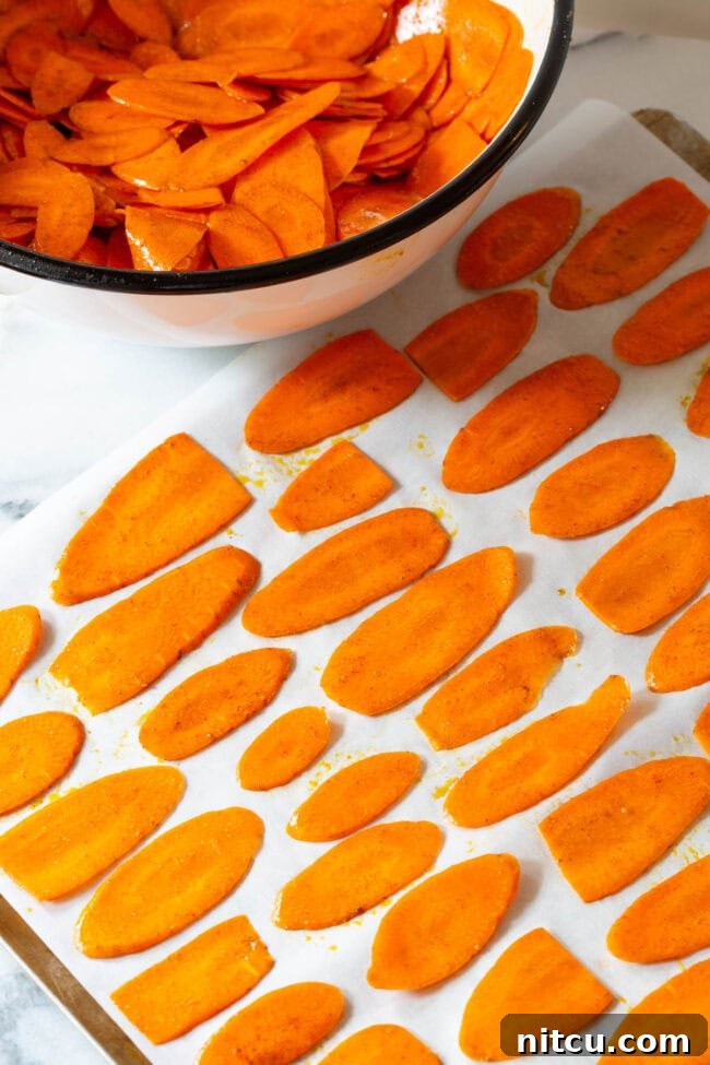 Crunchy Carrot Crisps 7 Seasoned carrot slices spread in a single layer on a baking sheet.