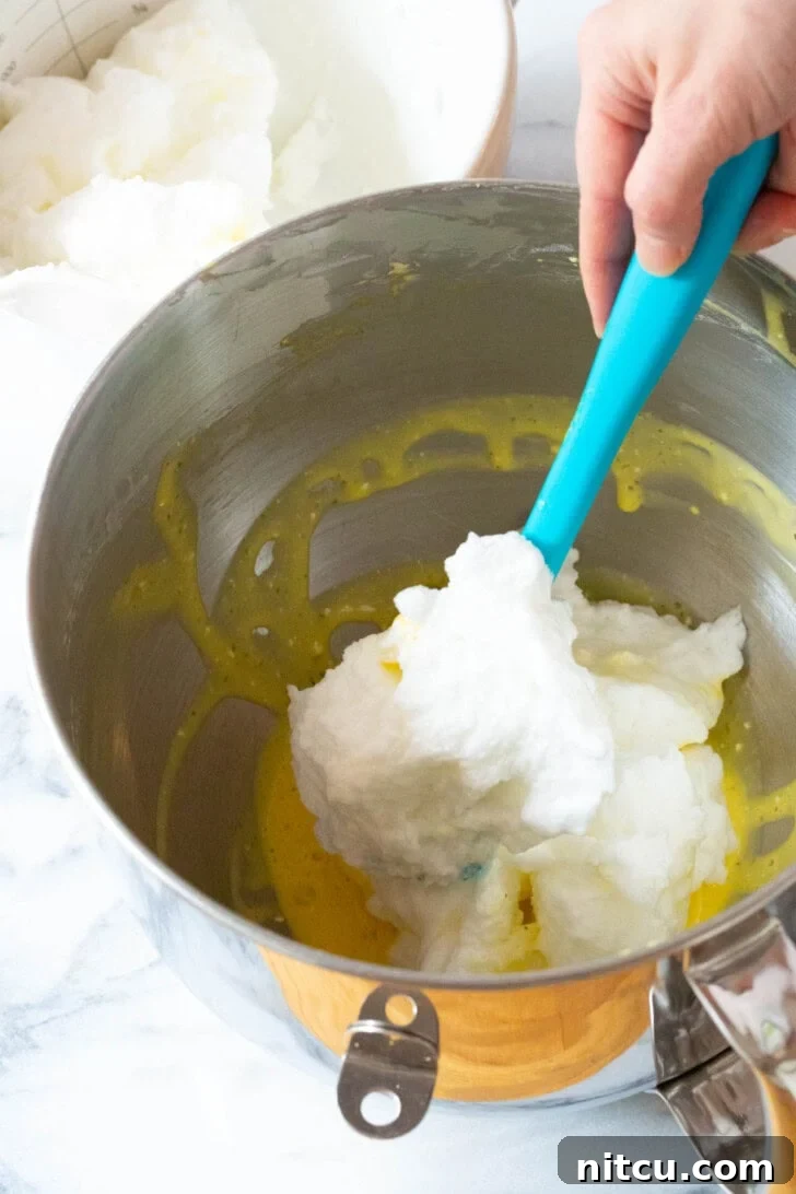 Fluffy Egg Mixture #LowCarb #GlutenFree #GrainFree #Keto #CloudBread #KetoCloudBread #NoCarbBread The process of gently folding whipped egg whites into the rich egg yolk mixture, demonstrating a key step for airy cloud bread.