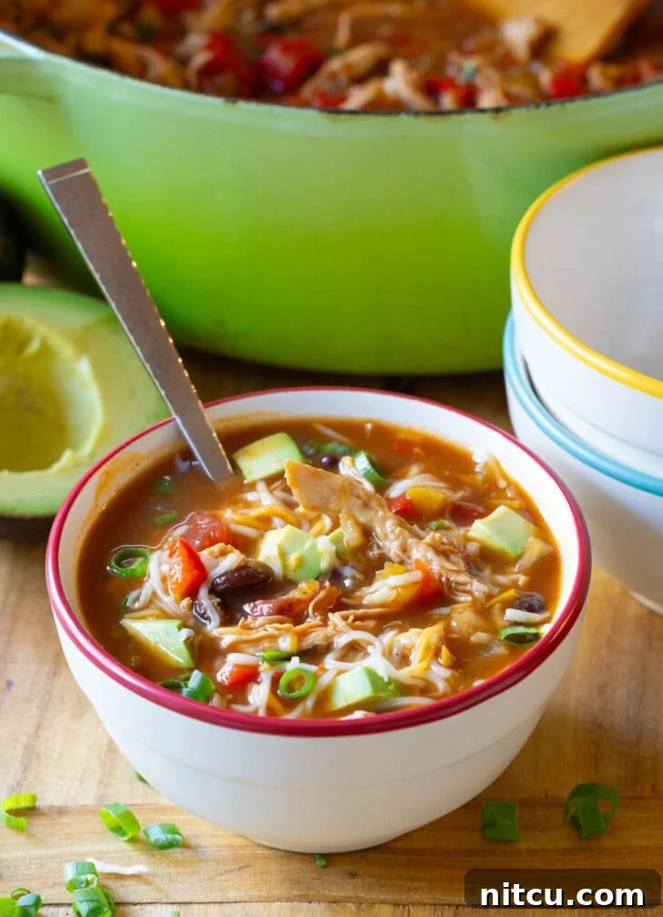 Delicious Chicken Fajita Soup Soup in a bowl garnished with melted shredded cheese, vibrant sliced scallions, and creamy diced avocado, ready to be enjoyed.