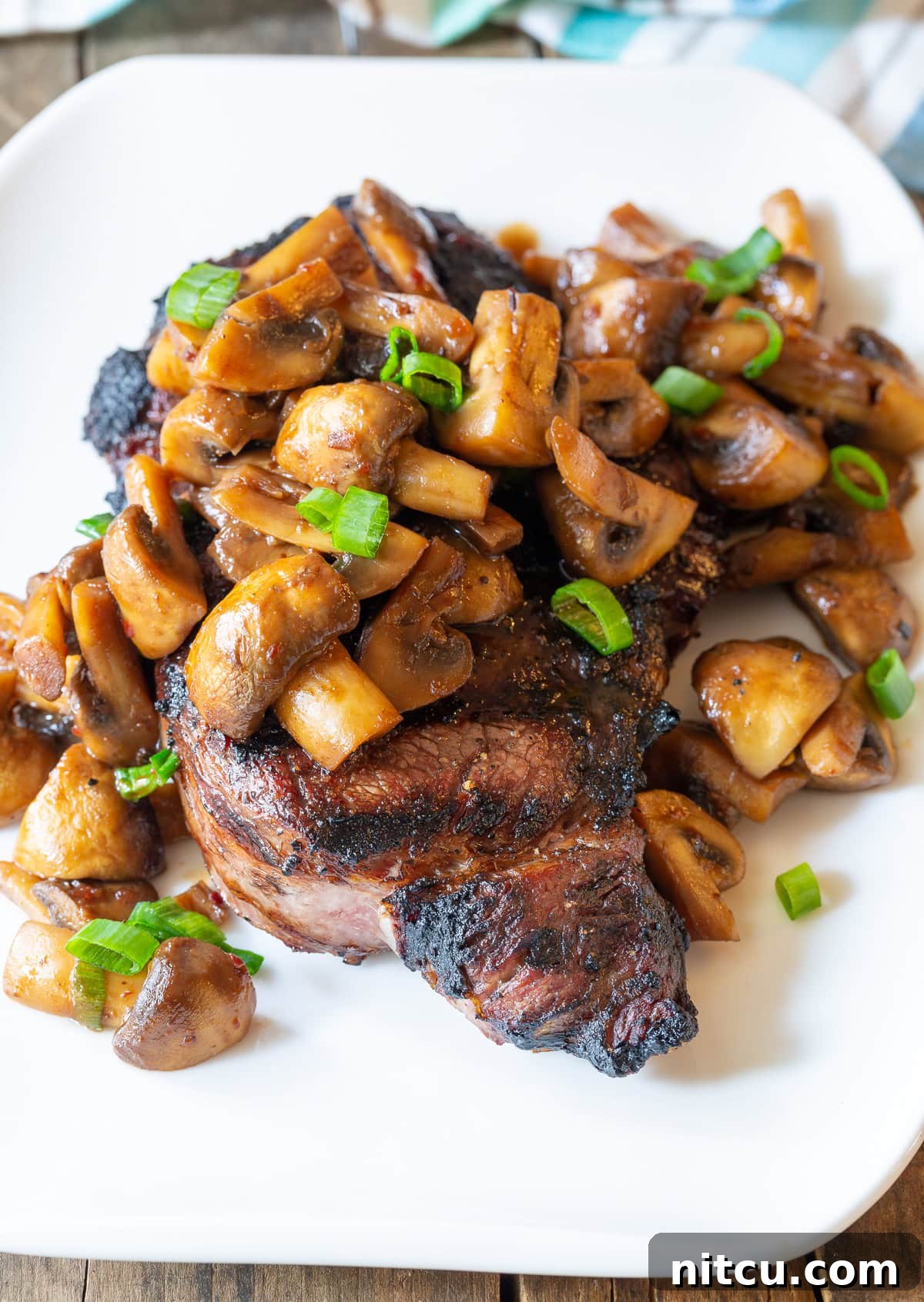 Mushroom Stir Fry #ASpicyPerspective #Mushrooms #StirFry #MushroomStirFry #AsianMushroom #Asian #SideDish #Vegetarian #Healthy #LowCarb #LowFat Stir-fried Asian-style mushrooms served over a steak on a white plate.
