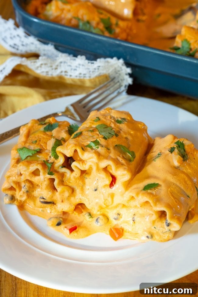 Spicy Southwest Chicken Lasagna Spirals 11 Three perfectly baked Southwest chicken lasagna roll ups on a white plate with a silver fork, ready to eat.