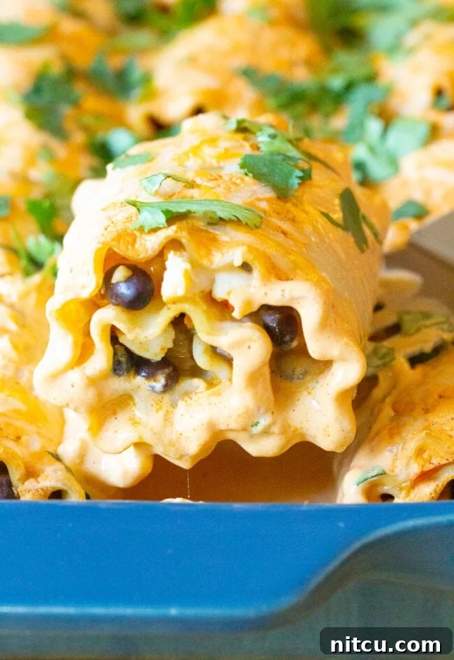 Spicy Southwest Chicken Lasagna Spirals 4 A spatula lifting a southwest lasagna roll up from a blue baking dish, showing the cheesy filling.