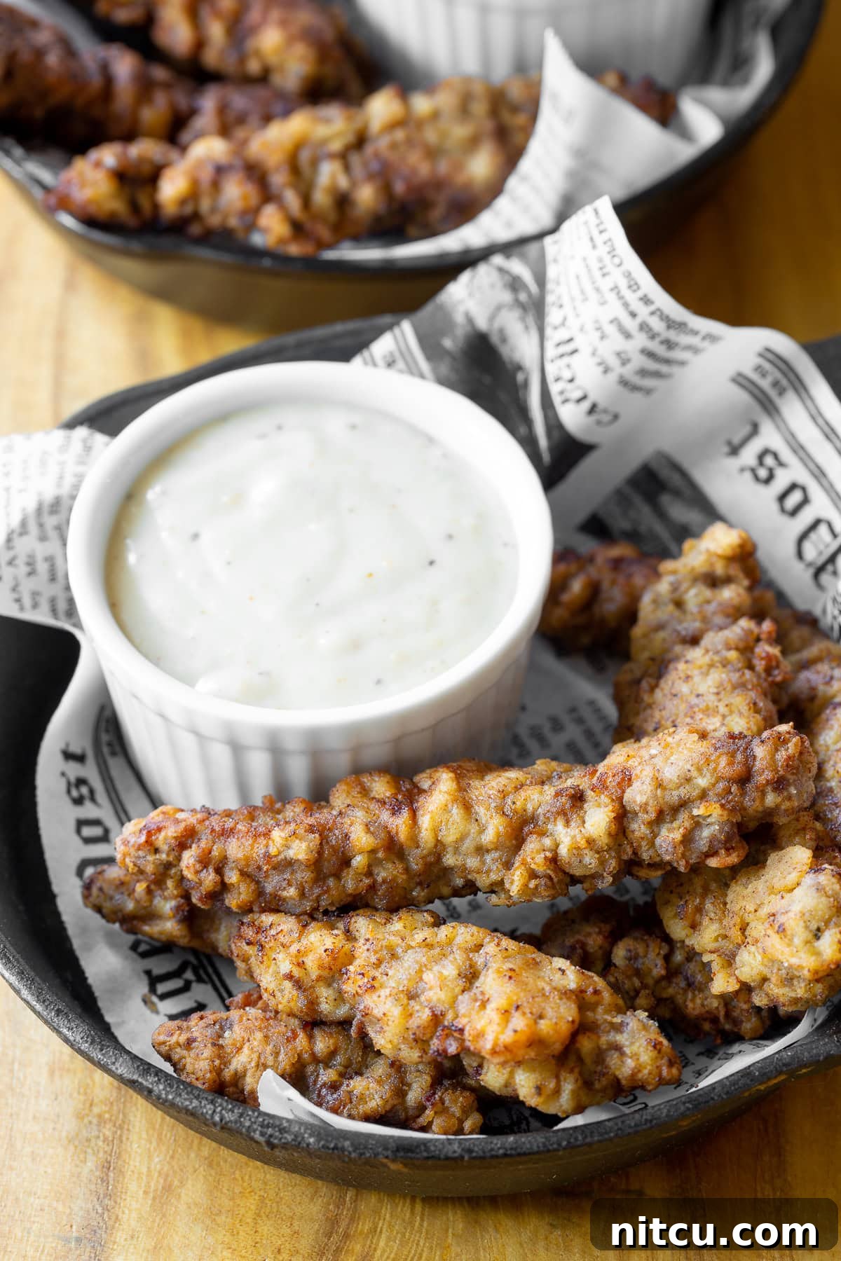 Beef Tenders 2 Crispy steak fingers served in a cast iron plate with a side of creamy country gravy for dipping.